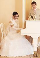 bride playing a white piano with groom standing beside her